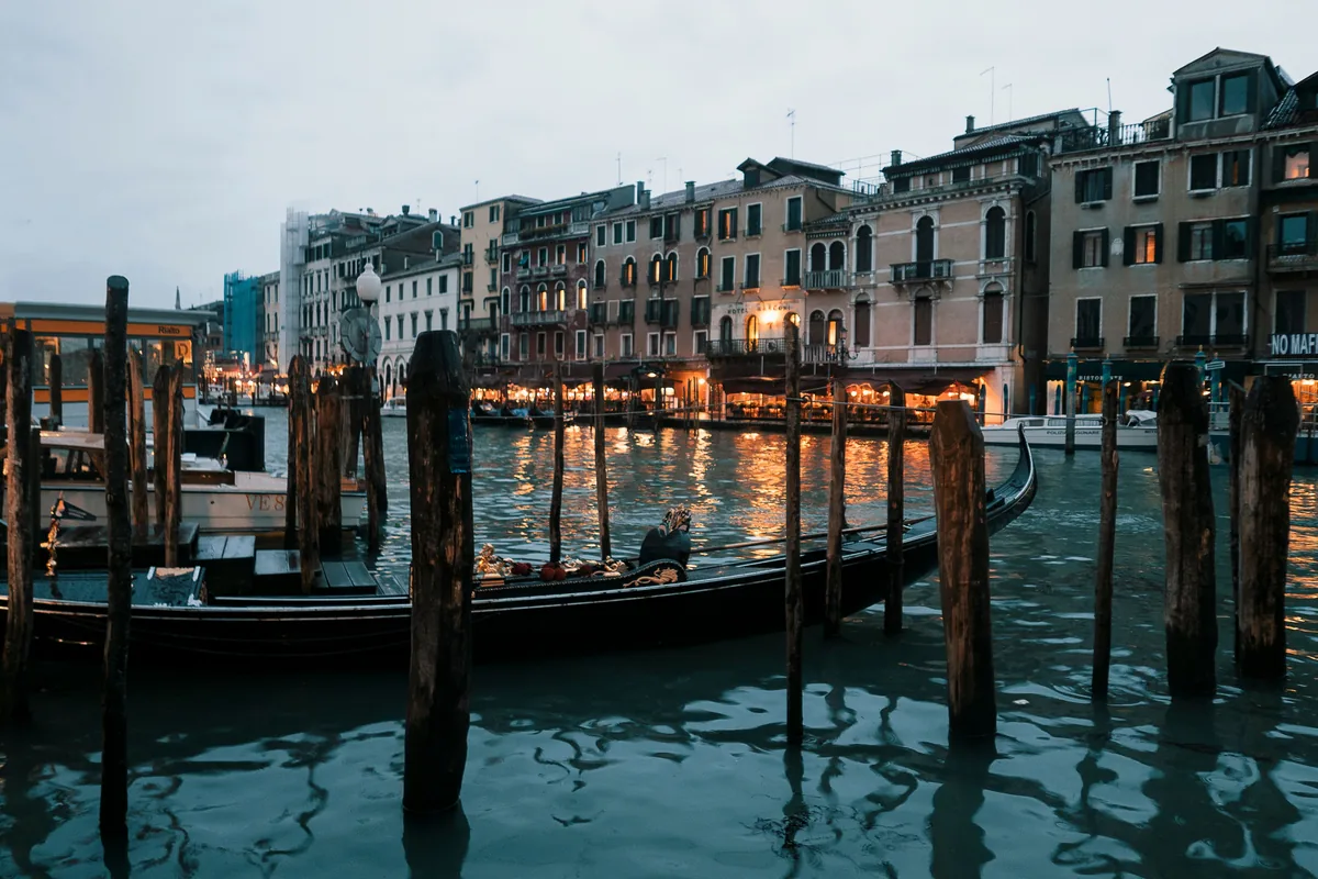 Una gondola ormeggiata in un canale di Venezia al crepuscolo, con le finestre illuminate dei palazzi che si riflettono sull'acqua, emblema della Venezia notturna.